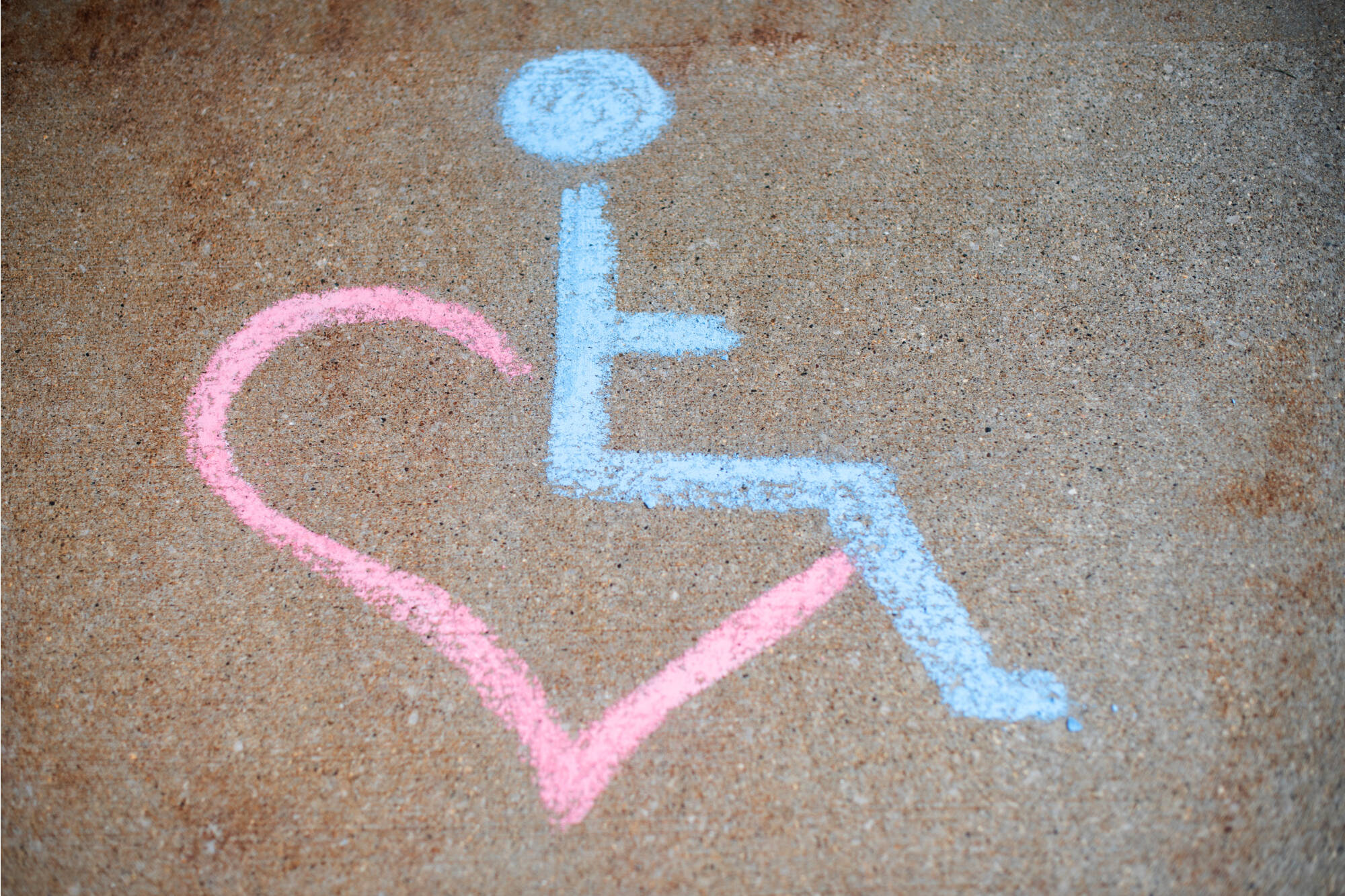 Chalk drawing of an accessibility symbol within a pink heart on concrete.